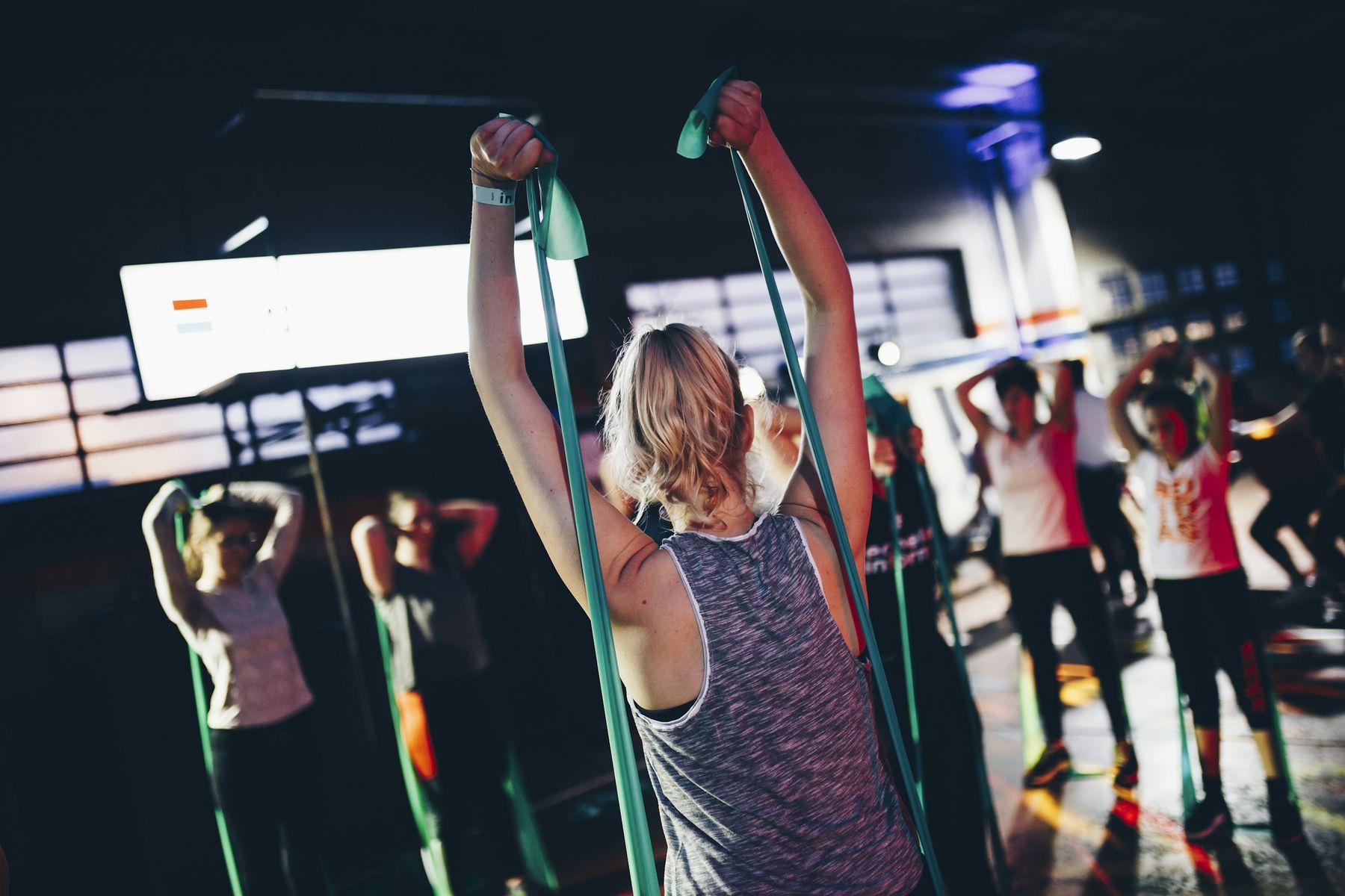 A group fitness class works through resistance-band overhead presses in a moody, backlit studio.